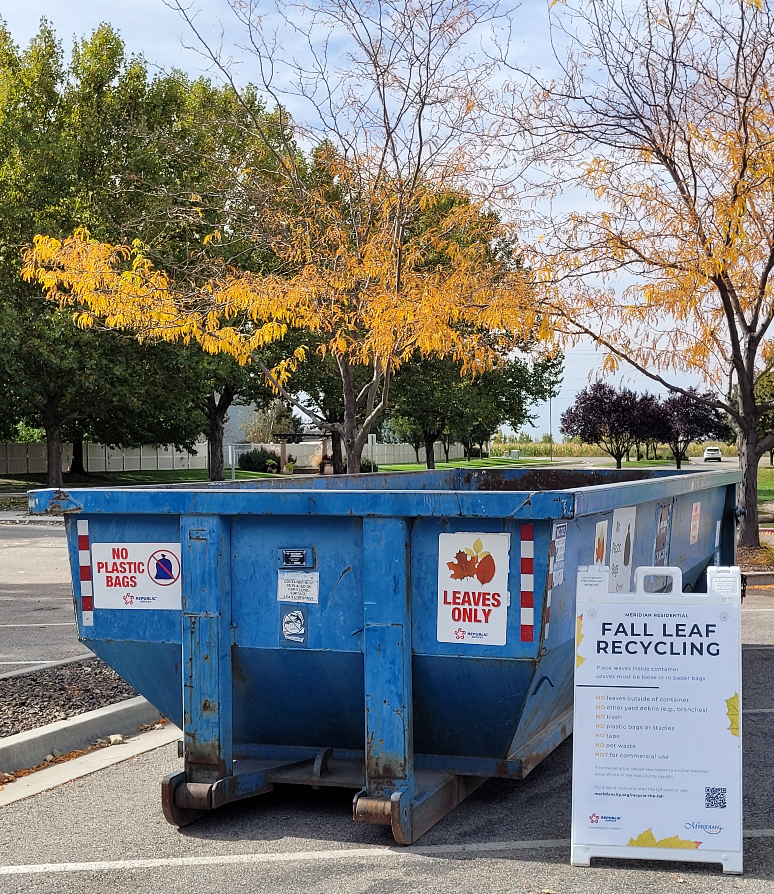 Large blue roll off bin with a Leaves Only sign and a Recycle the Fall a frame to the right of it (words not legible)